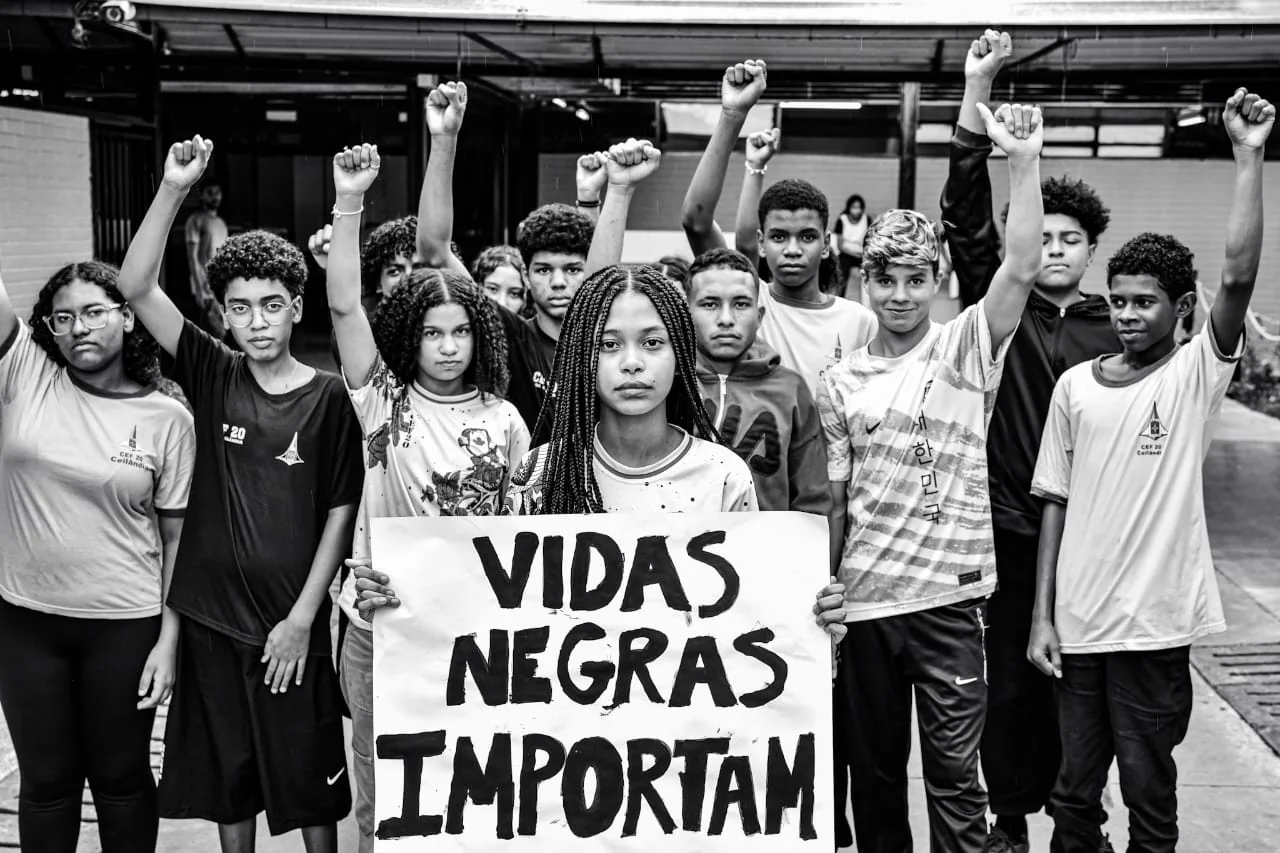 Estudantes negros erguem os punhos; ao centro, uma jovem segura o cartaz Vidas Negras Importam