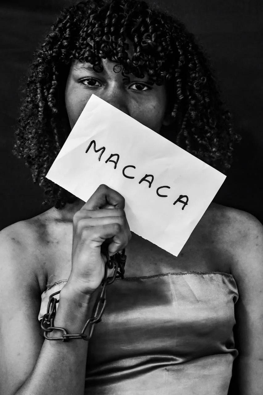 Jovem segura diante da boca um papel com a palavra Macaca, em denúncia ao racismo