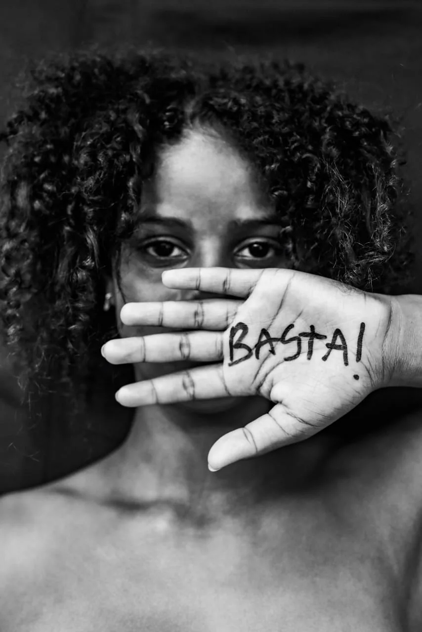 Jovem ergue a mão com a palavra Basta escrita na palma