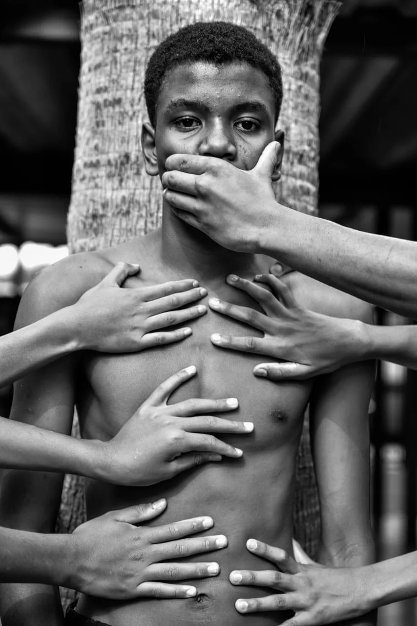 Jovem tem a boca coberta por uma mão enquanto outras mãos o tocam