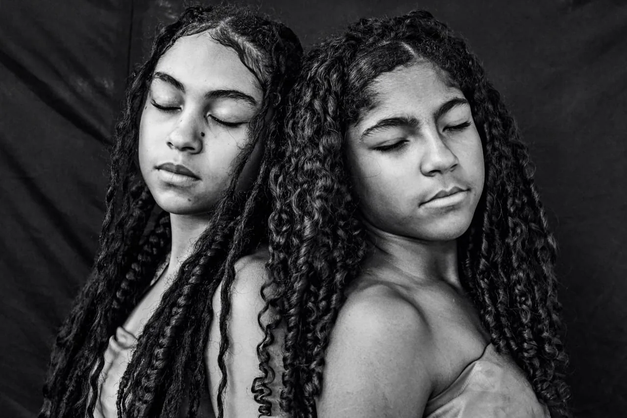 Duas jovens de olhos fechados aparecem lado a lado em retrato sobre identidade e pertencimento